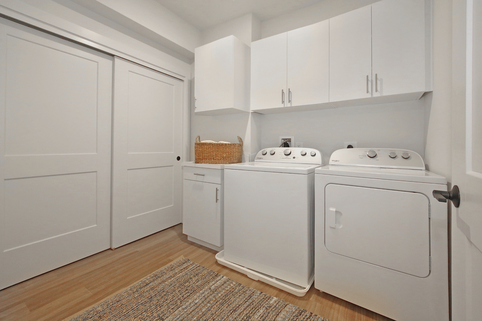 Modern laundry room with sleek white cabinetry, state-of-the-art washer and dryer, and stylish wood flooring.