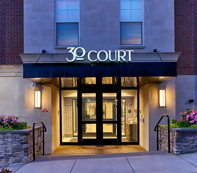 Chic entrance of 30 Court featuring modern architecture, ambient lighting, and decorative flower beds.