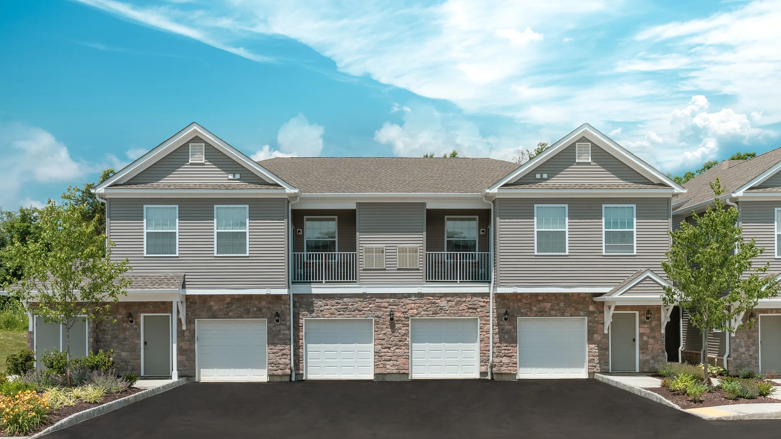 Charming duplex with modern stone facade, featuring two-story design and individual garages, set against a bright blue sky.