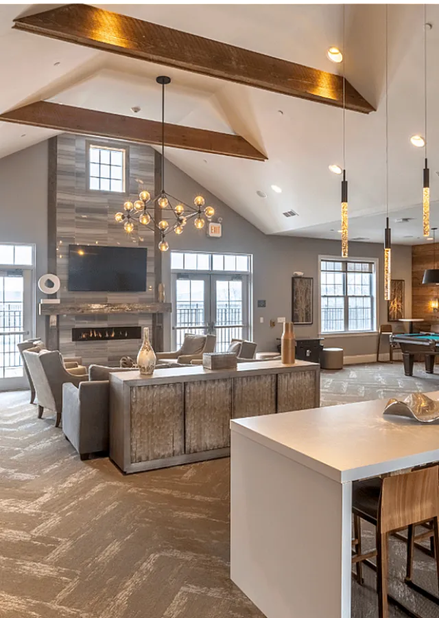 Chic and spacious lounge area featuring modern lighting, comfortable seating around a fireplace, a billiards table, and a stylish bar with high stools.