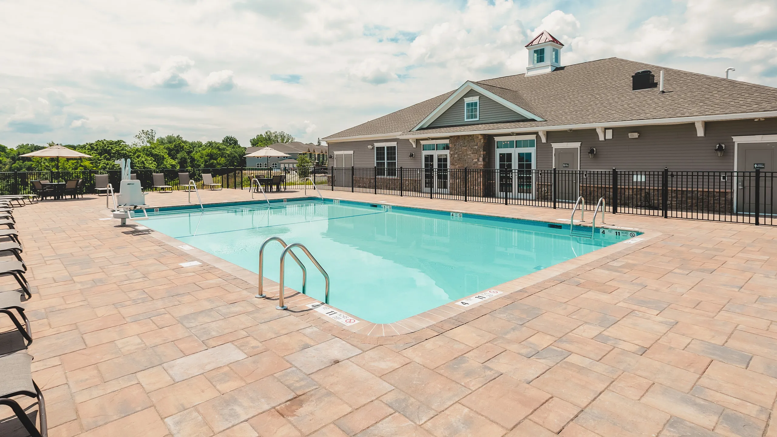 Inviting outdoor pool area with modern lounge chairs, set against a scenic backdrop of greenery and a charming clubhouse.