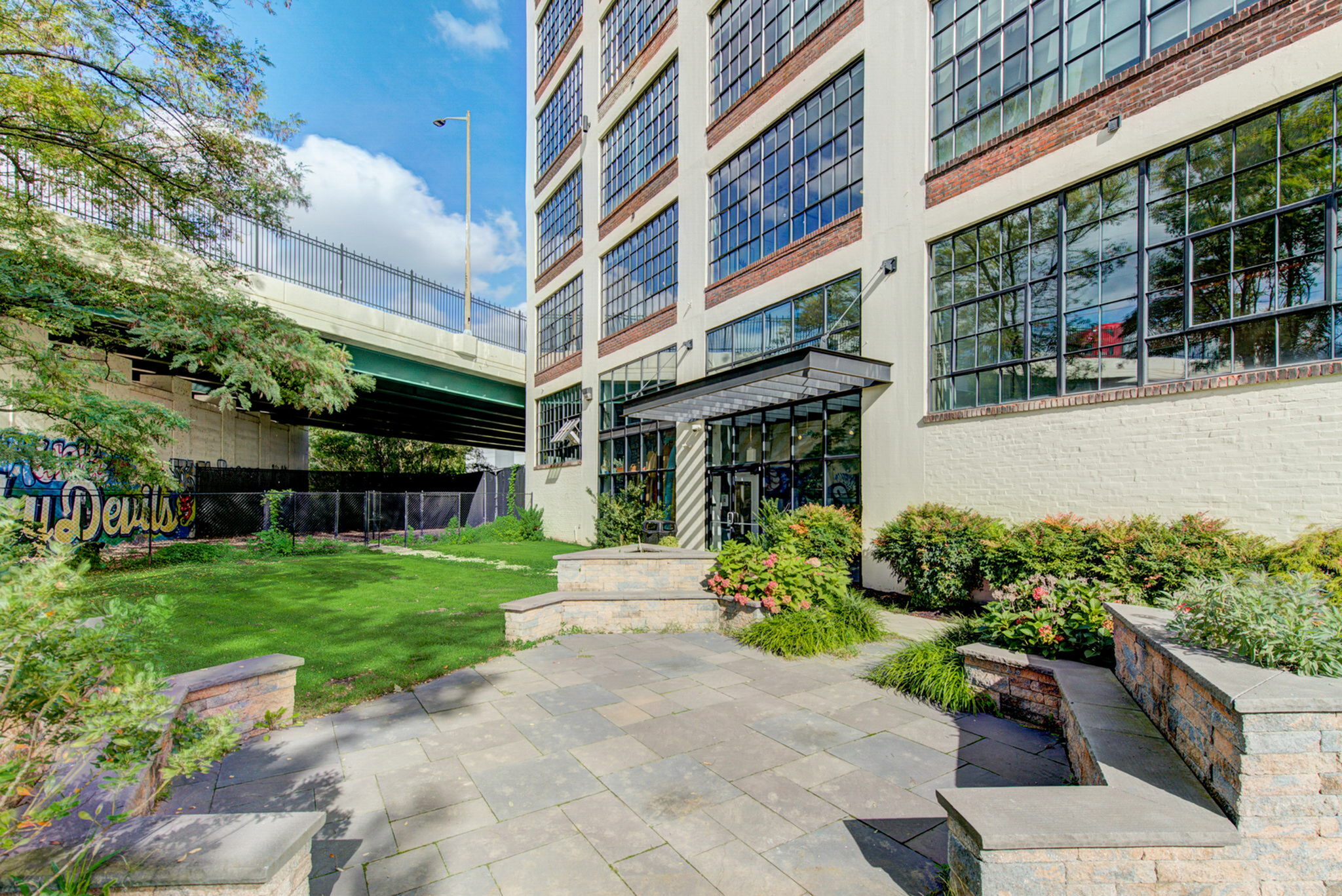 Charming urban apartment building with large windows, lush landscaping, and a vibrant graffiti mural nearby, offering a perfect blend of modern living and artistic flair.