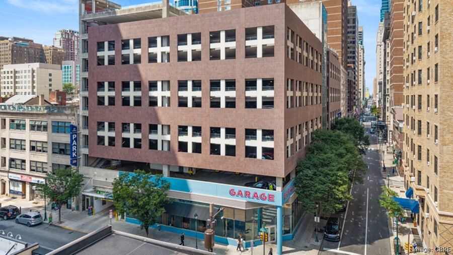 Vibrant city street with a modern multi-level parking garage, surrounded by towering buildings and lush greenery, offering convenience and accessibility.