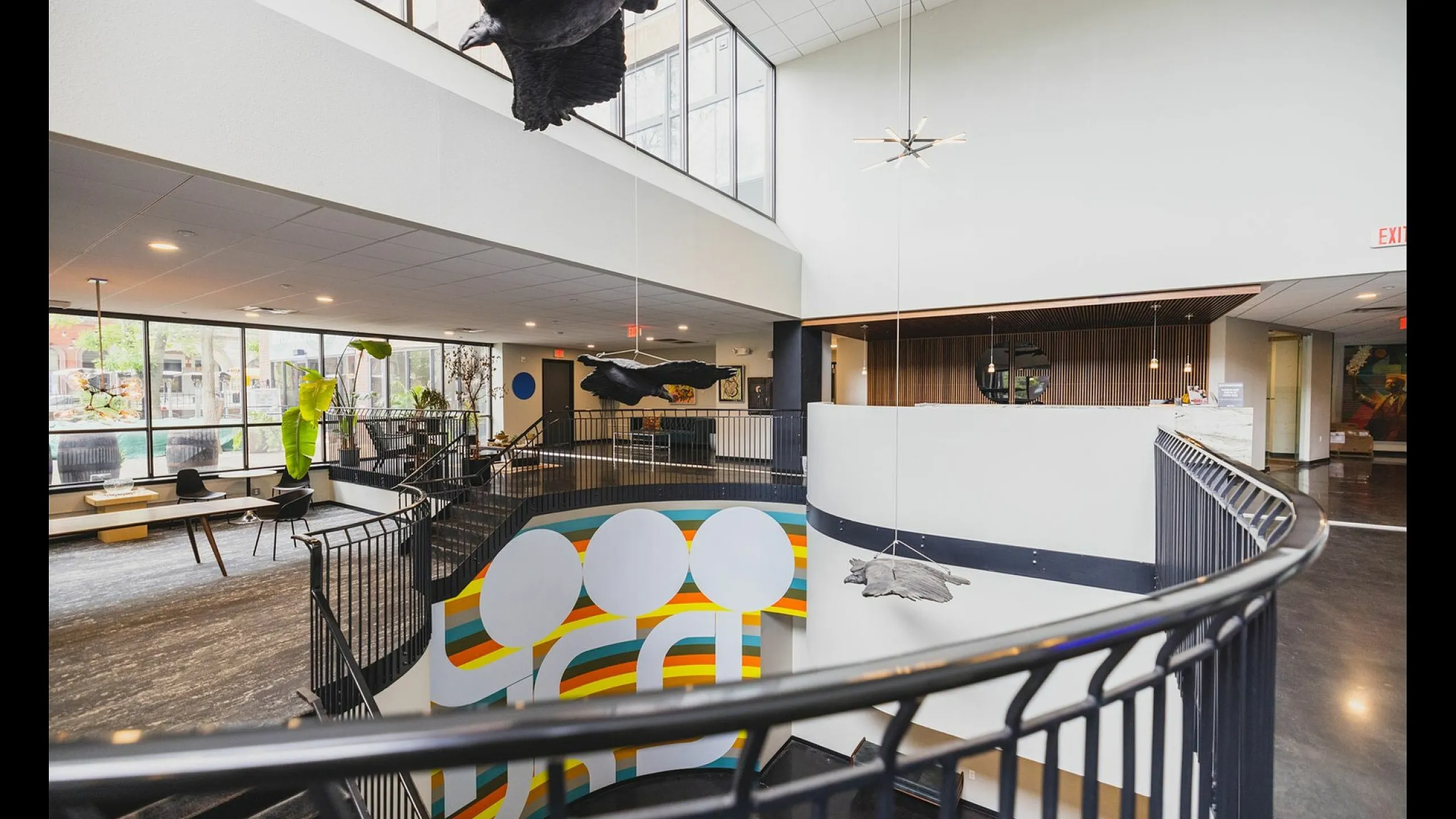 Stylish atrium with vibrant mural and suspended bird sculptures, featuring large windows and sleek railing.