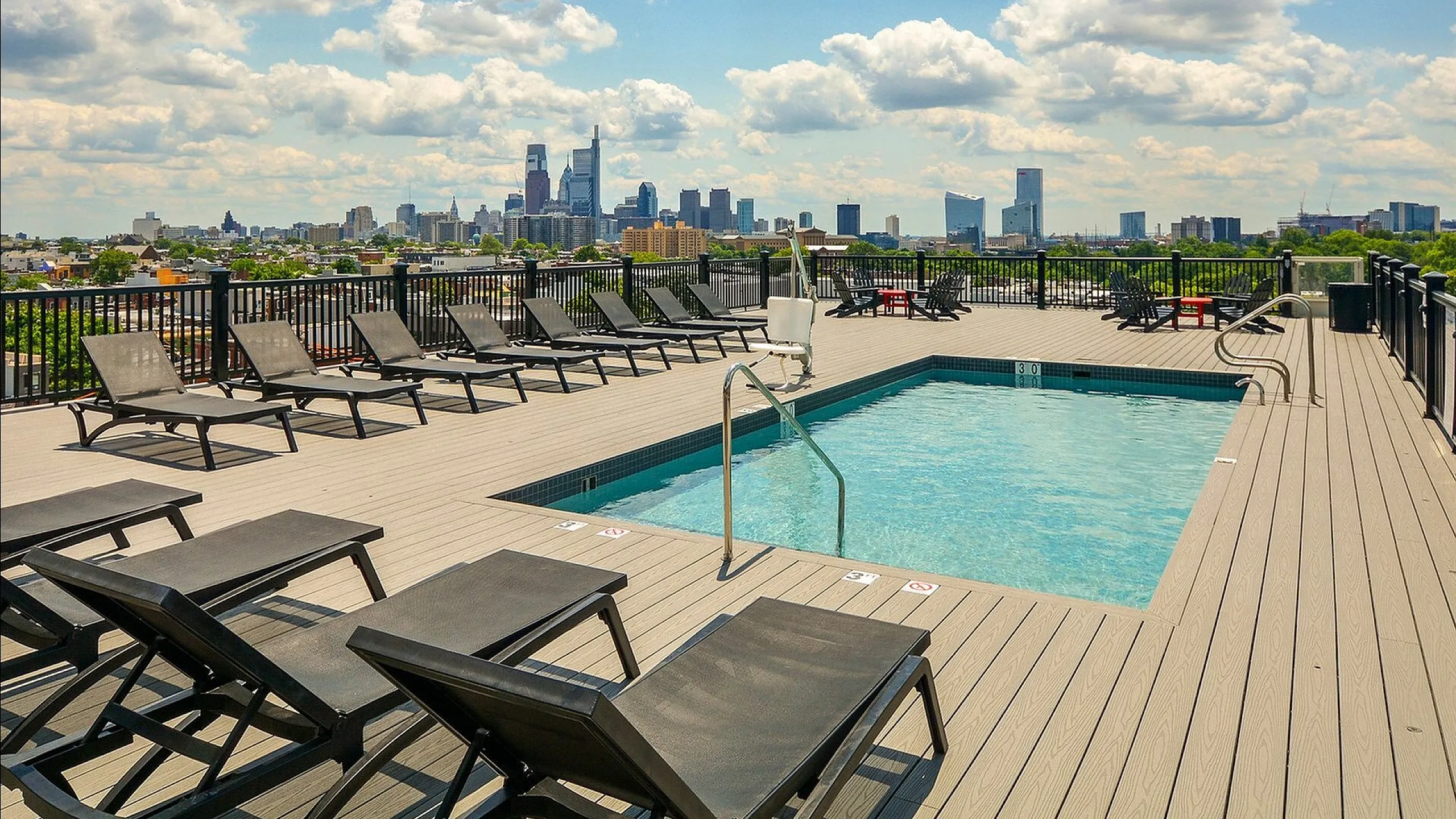 Rooftop plunge pool deck featuring lounge chairs and city skyline in the background.