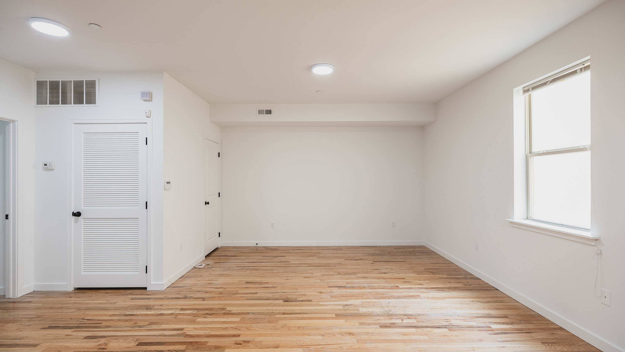 Bright and airy room with elegant hardwood floors and ample natural light from a large window, perfect for a cozy space.