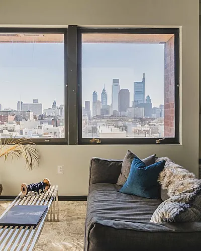 Chic urban living room with cozy seating and stunning city skyline views through large windows.