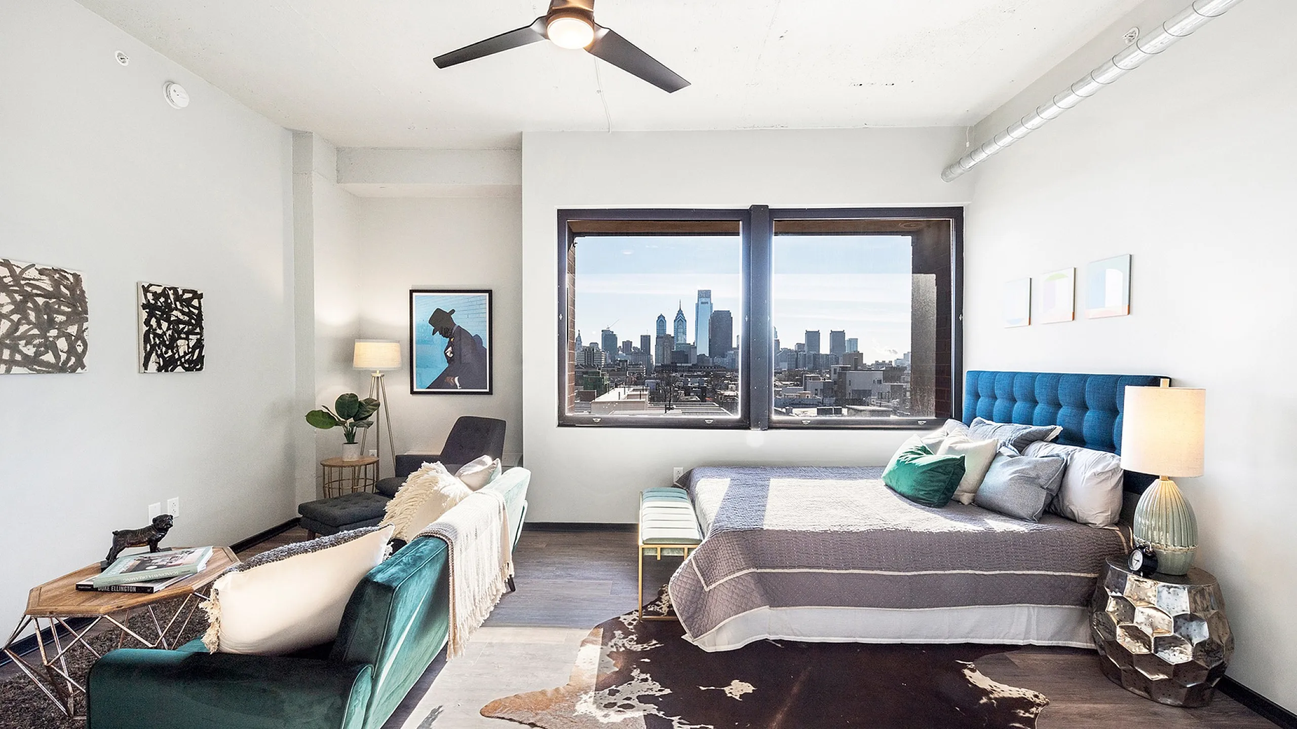 Modern apartment bedroom with stylish decor, offering breathtaking city skyline views through large windows. Features elegant furnishings and a cozy seating area.