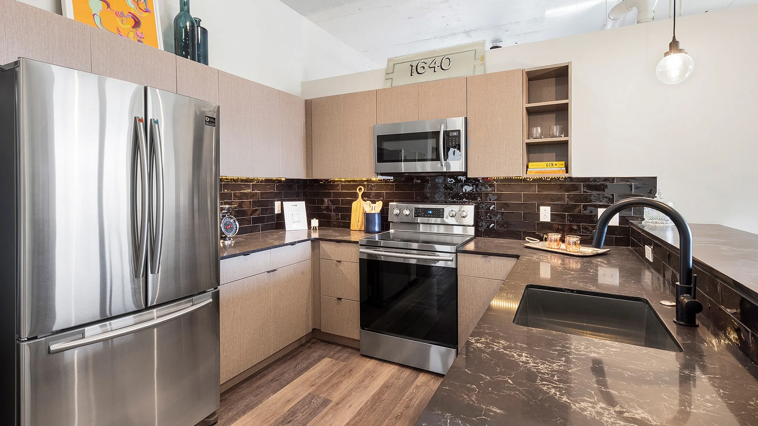 Contemporary kitchen design featuring sleek stainless steel appliances, glossy black tile backsplash, and elegant marble-countered island.