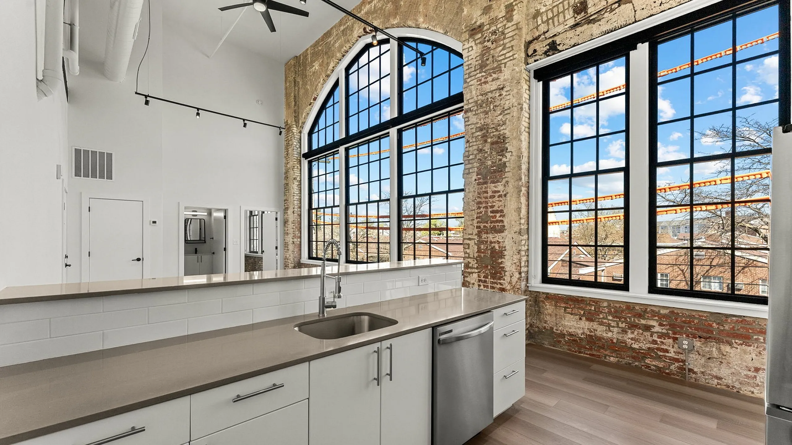 Chic industrial kitchen with exposed brick walls, large arched windows, modern cabinetry, and a sleek countertop for an urban loft feel.