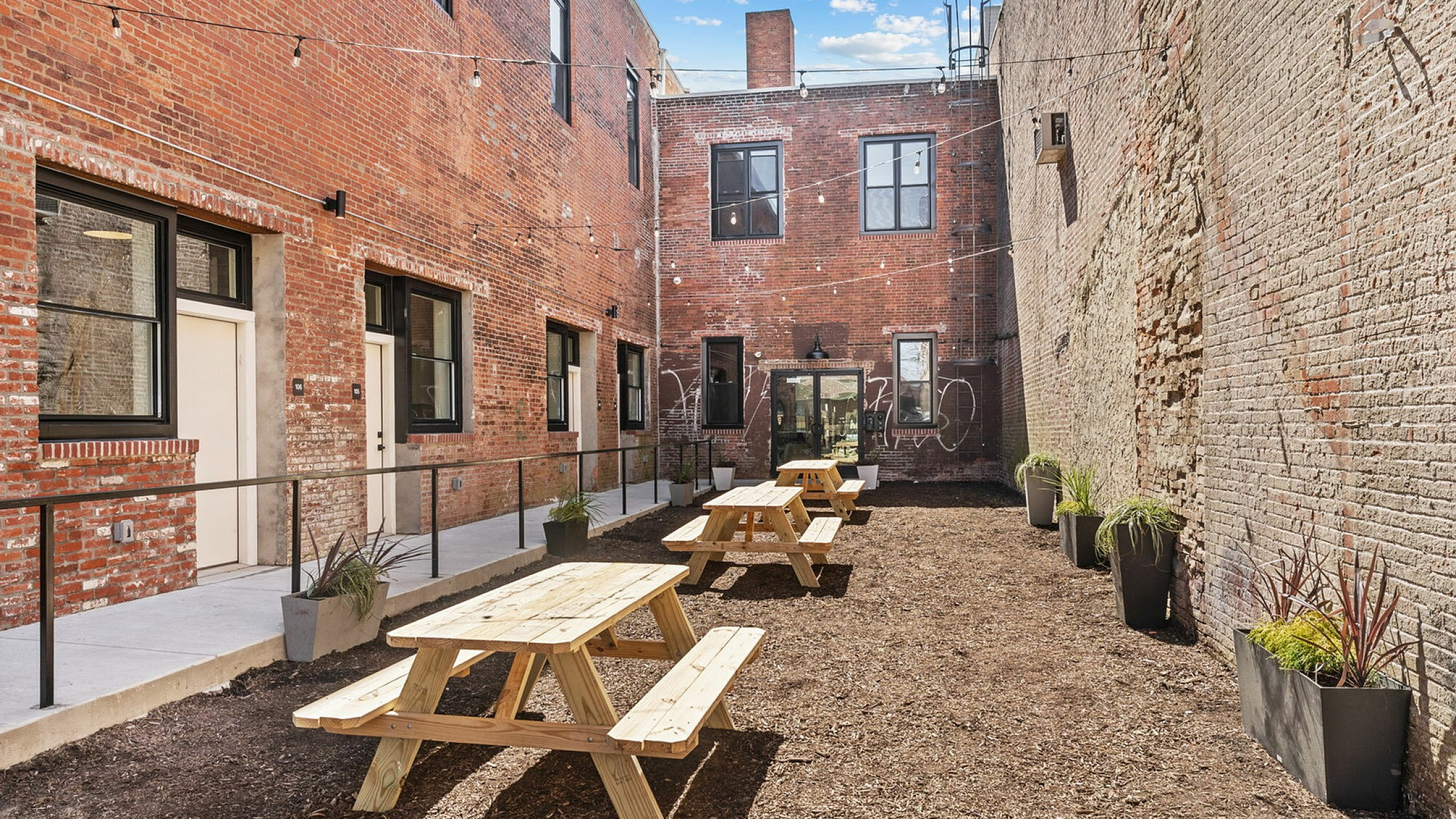 Inviting urban courtyard with picnic tables, surrounded by charming red brick walls, perfect for outdoor gatherings.