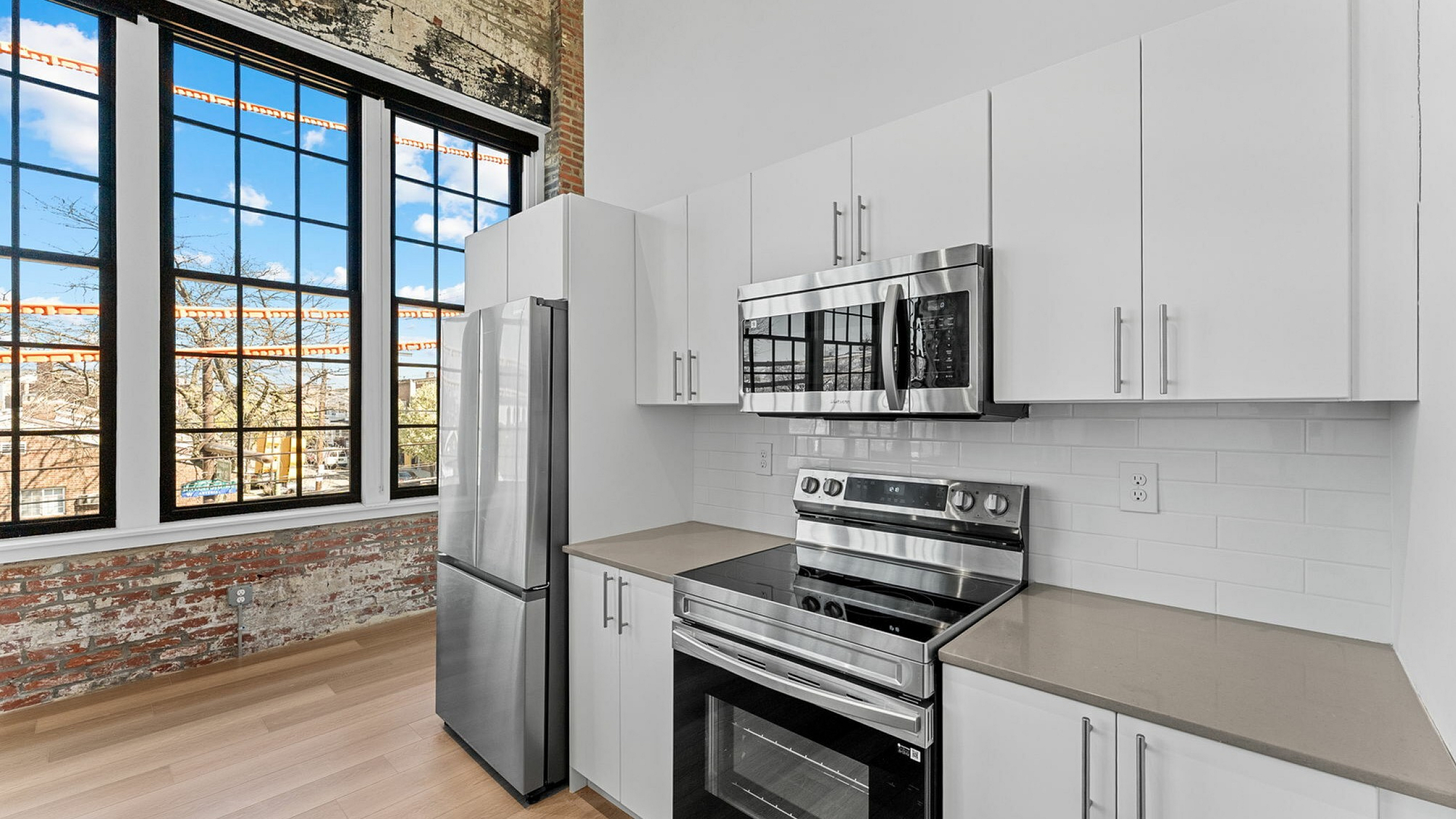 Chic modern kitchen featuring stainless steel appliances, sleek white cabinetry, and expansive industrial windows showcasing a scenic urban view.