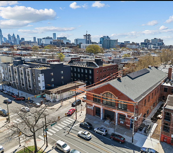 Charming urban neighborhood showcasing a blend of modern apartments and classic brick architecture, with a vibrant city skyline backdrop and clear blue skies.