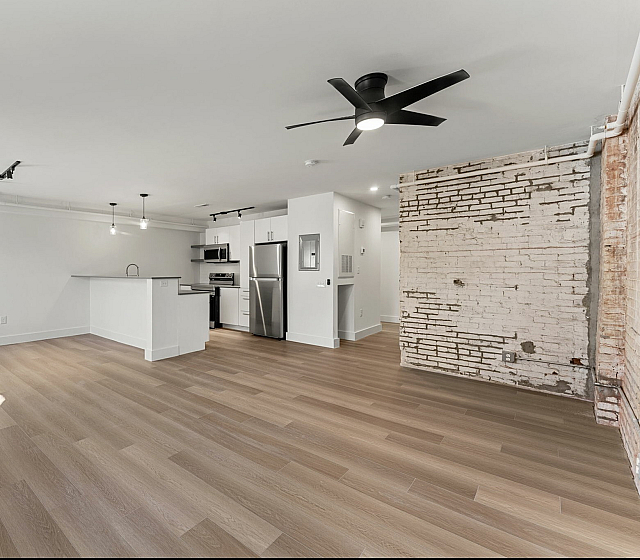 Contemporary open-plan living space with sleek kitchen, exposed brick accent wall, and modern lighting.