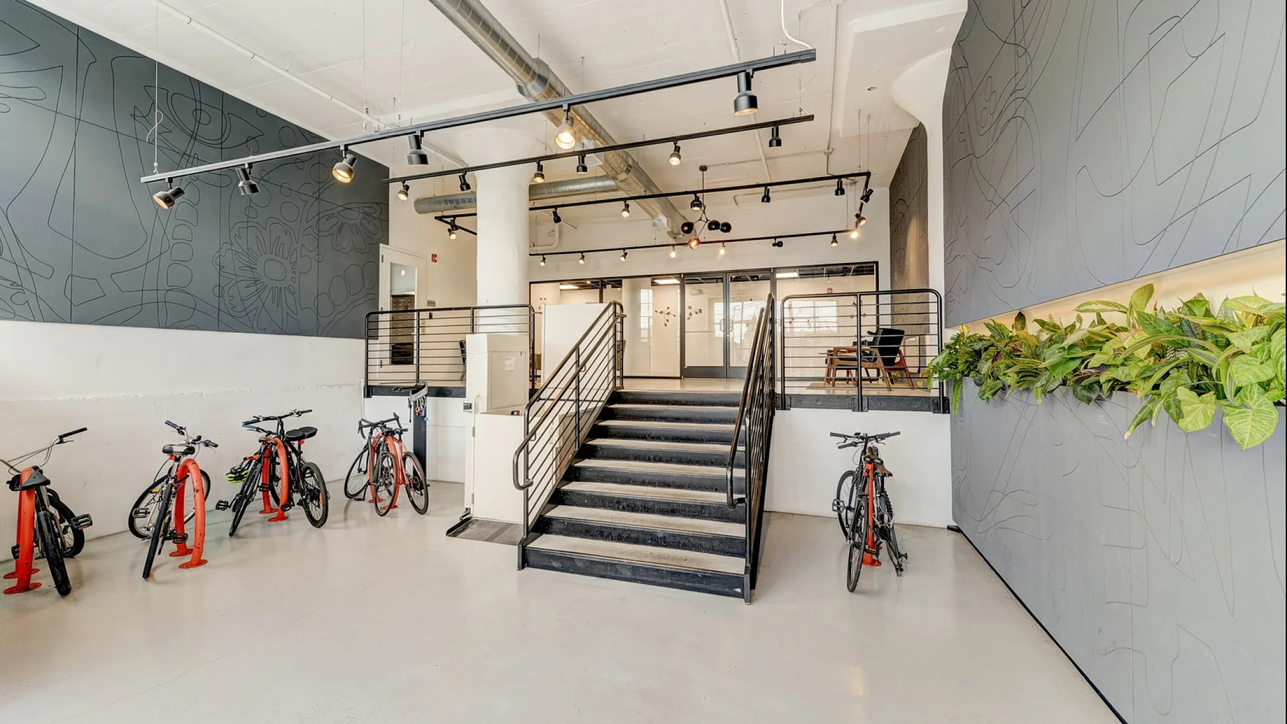 Modern communal space with sleek ceiling lights, artistic wall designs, indoor plants, and convenient bicycle storage.