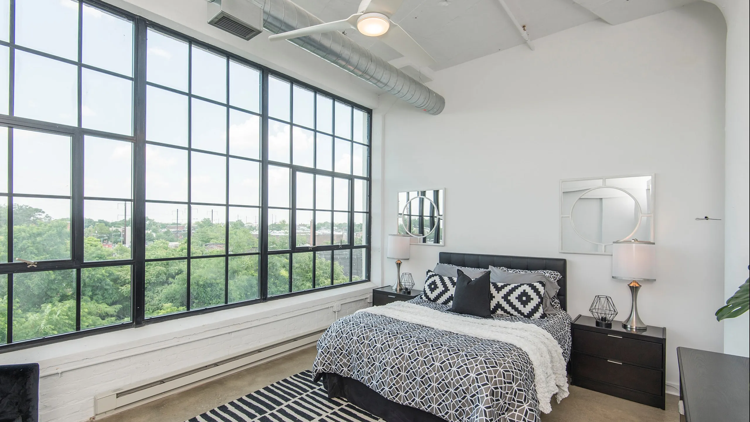 Chic bedroom with floor-to-ceiling windows offering lush views, modern decor, and stylish geometric accents.