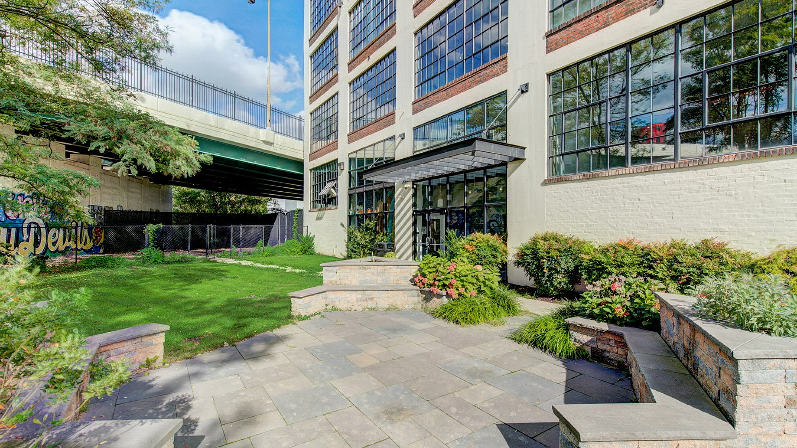 Charming modern apartment exterior with expansive windows, surrounded by lush greenery and a cozy patio area, perfect for urban living.