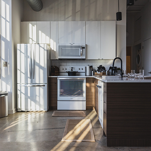 Bright modern kitchen with white cabinetry, sleek appliances, and large windows letting in natural light.
