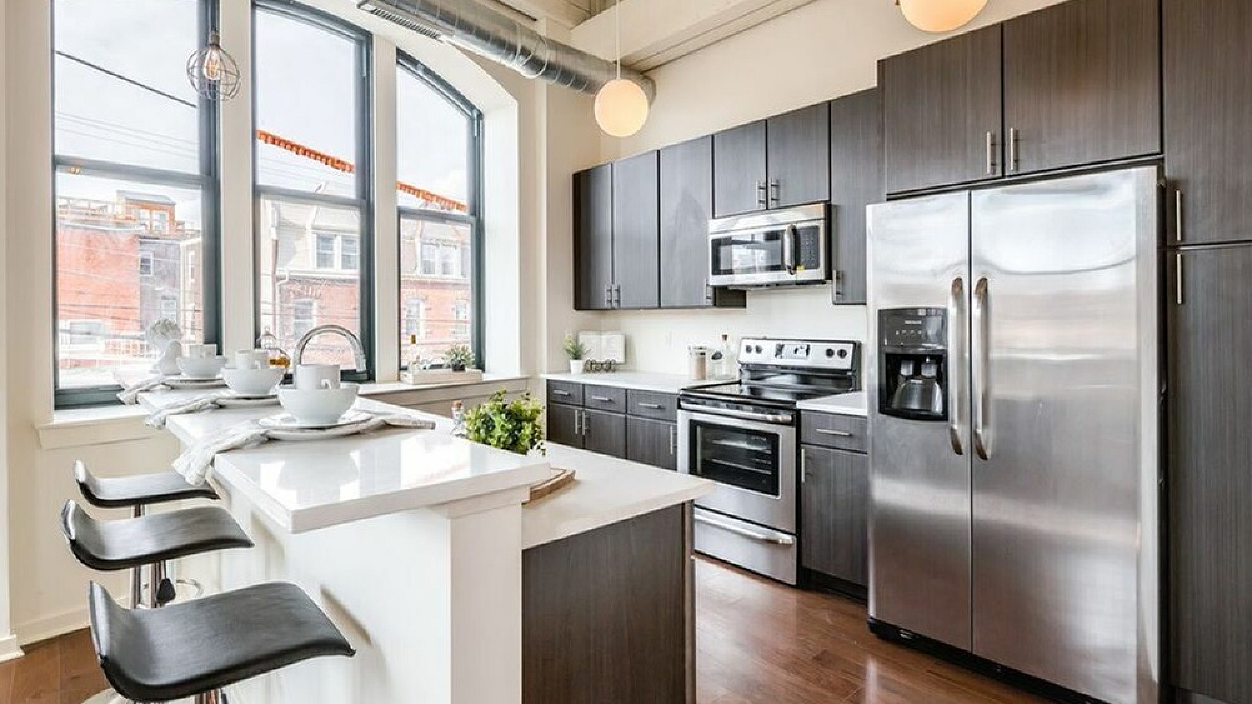 Chic modern kitchen with large windows, sleek dark cabinets, stainless steel appliances, and an inviting breakfast bar with stylish seating.