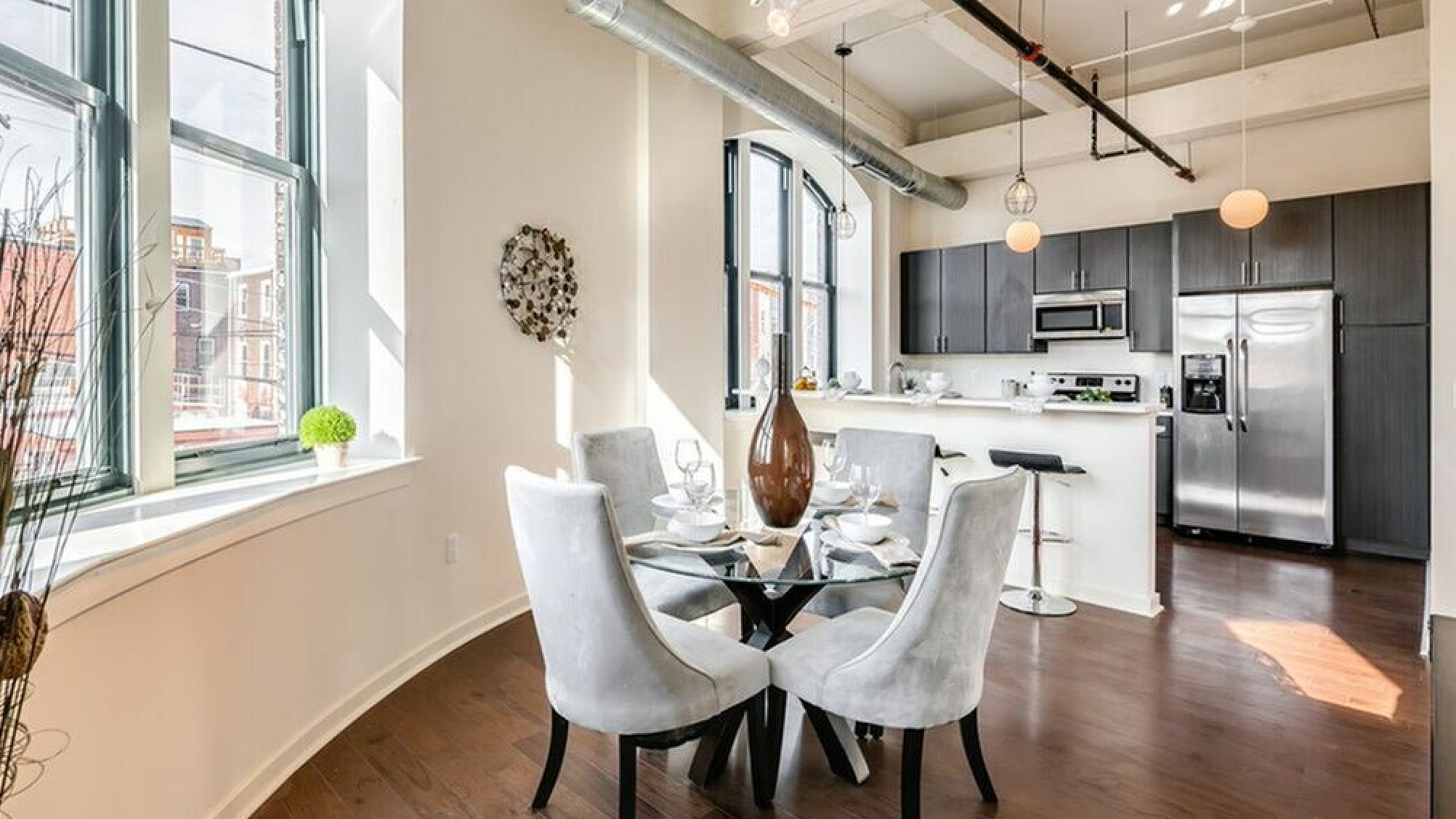 Bright and modern open-concept kitchen and dining area with large industrial windows, stylish decor, and sleek stainless steel appliances.