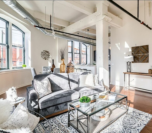 Bright loft apartment with chic industrial decor, highlighting large windows, an elegant seating area, and exposed beams.