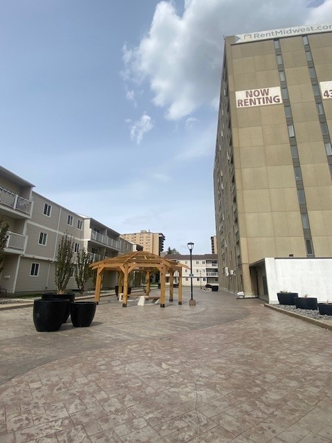 Inviting courtyard with stylish wooden pergolas and modern planters amidst apartment buildings, showcasing available rentals.