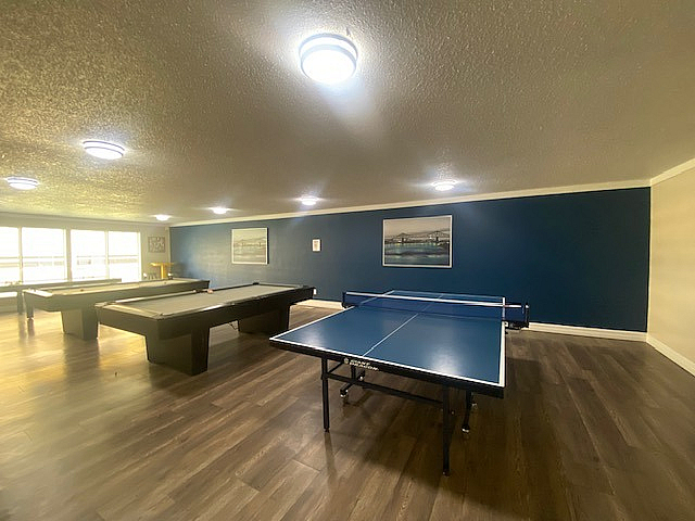 Modern recreational room featuring a ping pong table and two billiards tables, highlighted by stylish wooden flooring and ambient lighting.