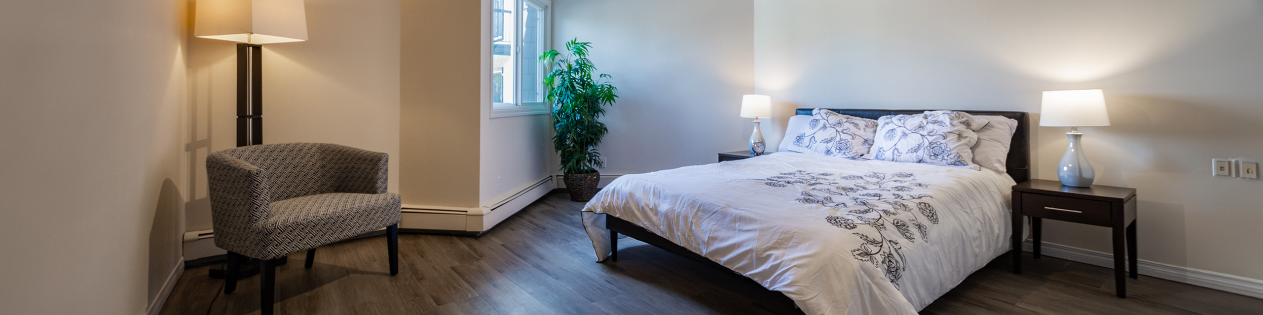 Elegant bedroom with a cozy double bed, stylish armchair, and soft lighting, complemented by lush greenery and modern decor.