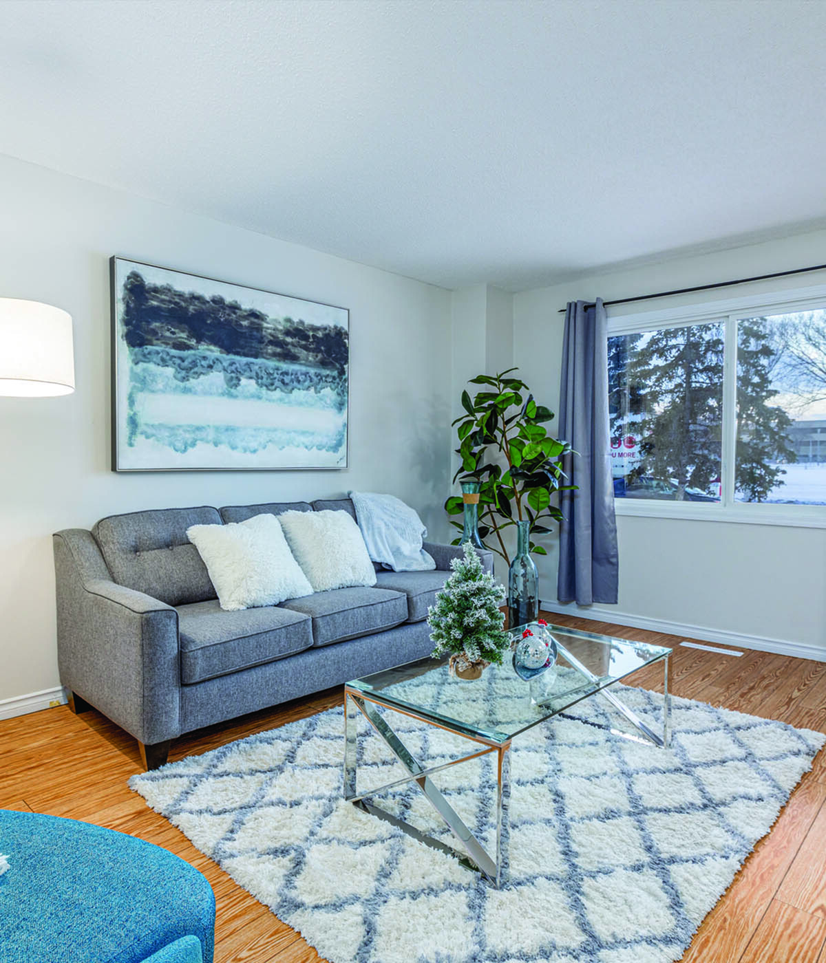 Bright and inviting living room featuring a modern gray sofa, elegant glass coffee table, and lush greenery with a large window view.