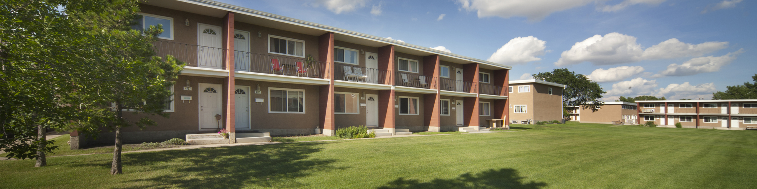 Sunny courtyard view of charming apartment complex with lush green lawn, balconies, and inviting outdoor spaces.