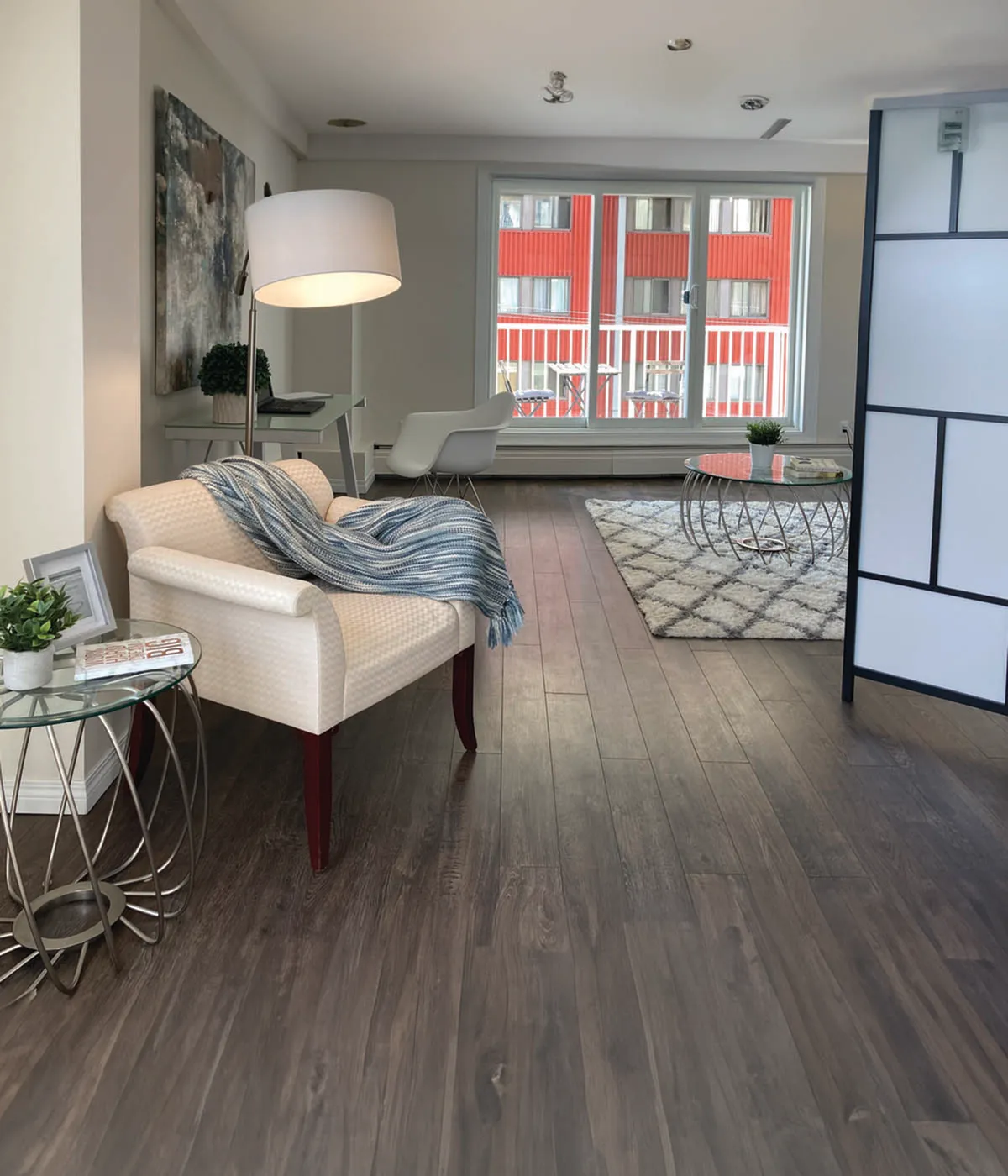 Elegant living space with modern decor, featuring a cozy armchair, stylish lamp, and a chic coffee table on a patterned rug, complemented by a bright window view.