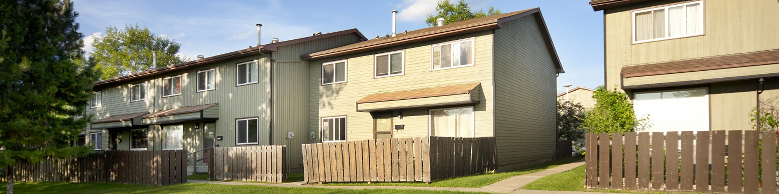 Charming townhouse exterior with contemporary design, fenced yards, and lush greenery, perfect for family living.