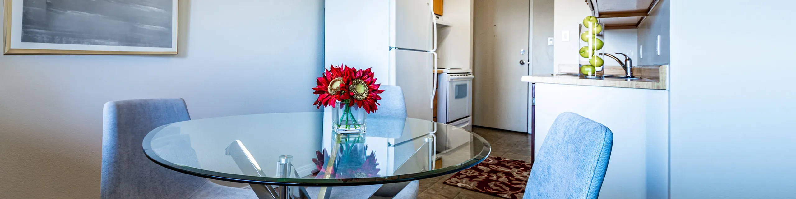 Charming dining area with a glass table, modern decor, and vibrant red flowers offering a cozy, inviting atmosphere.