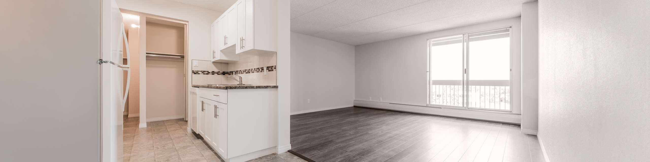 Modern apartment interior showcasing a sleek kitchen with white cabinets and open living area with large windows.