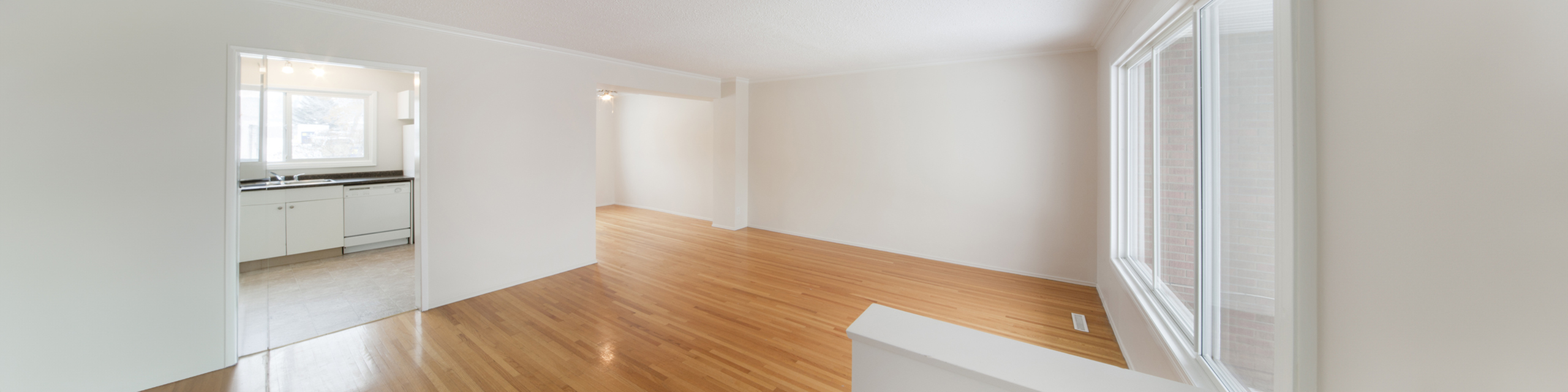 Bright and spacious living area with hardwood floors, large windows, and a modern kitchen, perfect for comfortable living and entertaining.