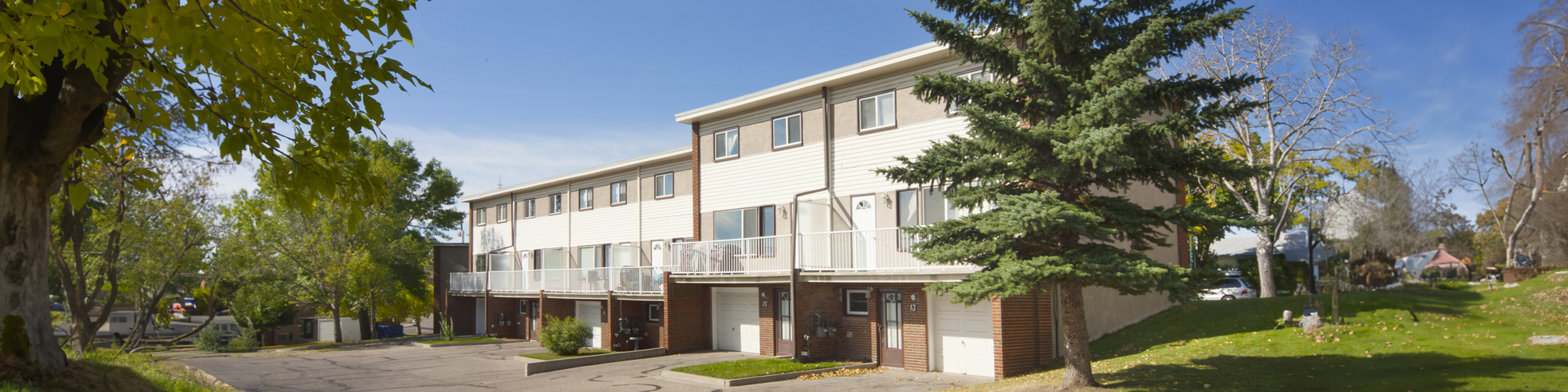 Charming townhouses with modern architecture nestled in lush greenery, featuring spacious exteriors and large garage spaces.