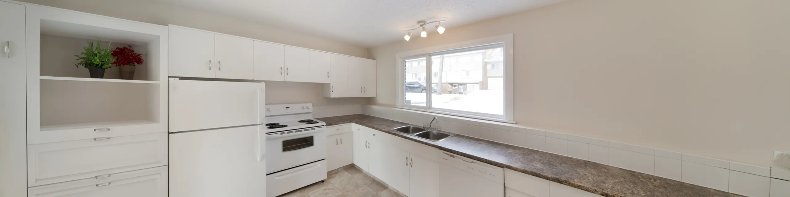 Bright and modern kitchen with sleek countertops, white cabinetry, and large window offering natural light.