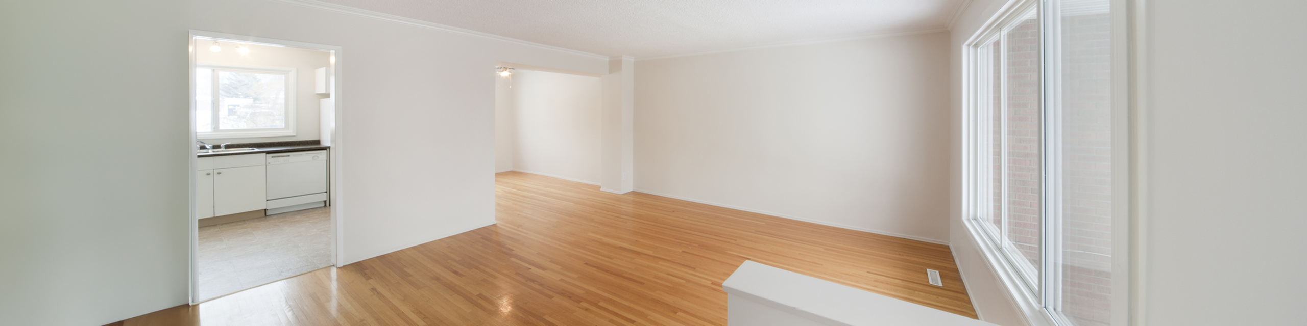 Bright and spacious living area with elegant hardwood flooring, large windows, and a glimpse into a modern kitchen.