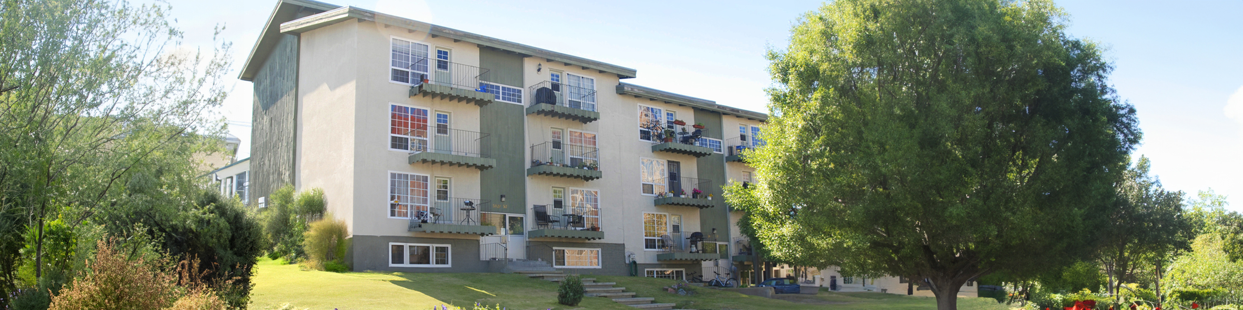 Charming apartment building surrounded by lush greenery, featuring private balconies and ample natural light, perfect for serene living.