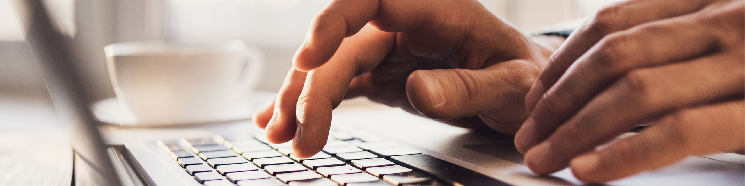 Close-up of hands typing on a laptop keyboard in a bright, modern setting.
