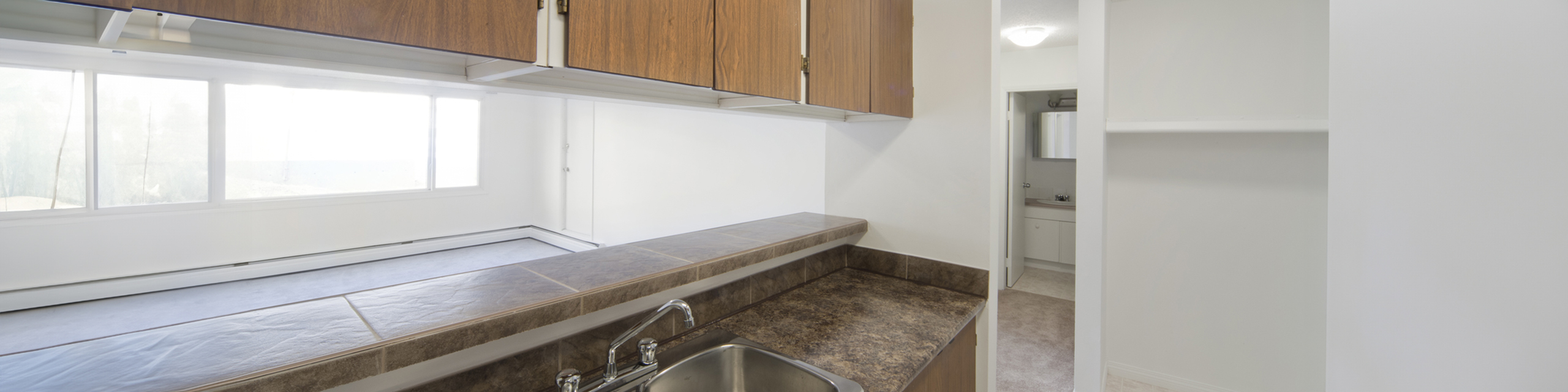 Bright kitchen with large windows, modern sink, and elegant cabinetry, leading to a cozy bathroom.