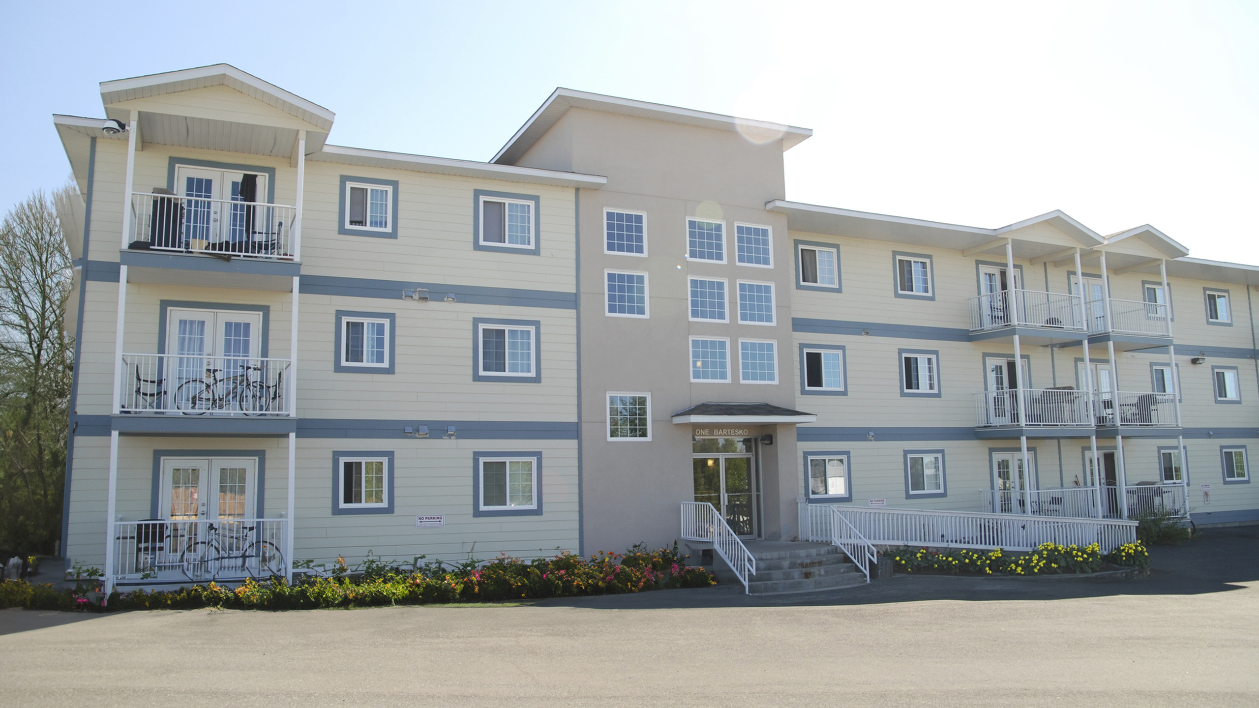 Charming modern apartment building with large sunny windows, inviting balconies, and lush landscaping.