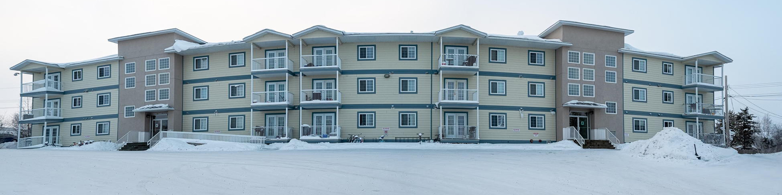 Modern apartment building with spacious balconies and stylish exterior, set in a serene snowy landscape.