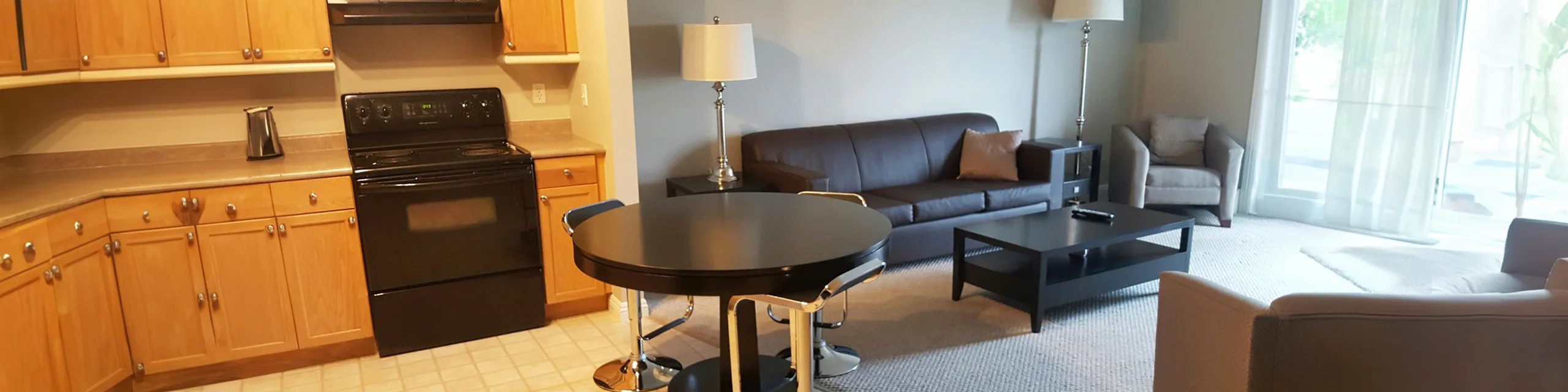 Inviting open-concept living area with a modern kitchen, cozy seating, and abundant natural light from large windows.