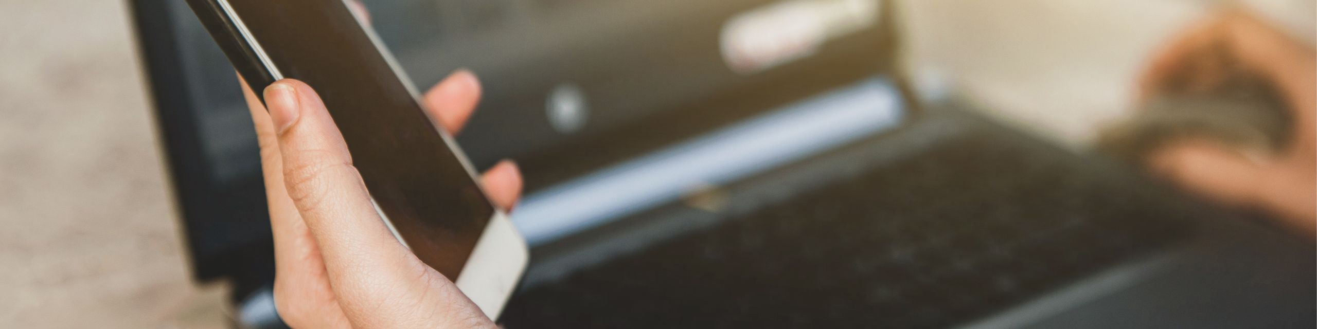 Close-up of hands working with a smartphone and laptop, showcasing a productive digital lifestyle.