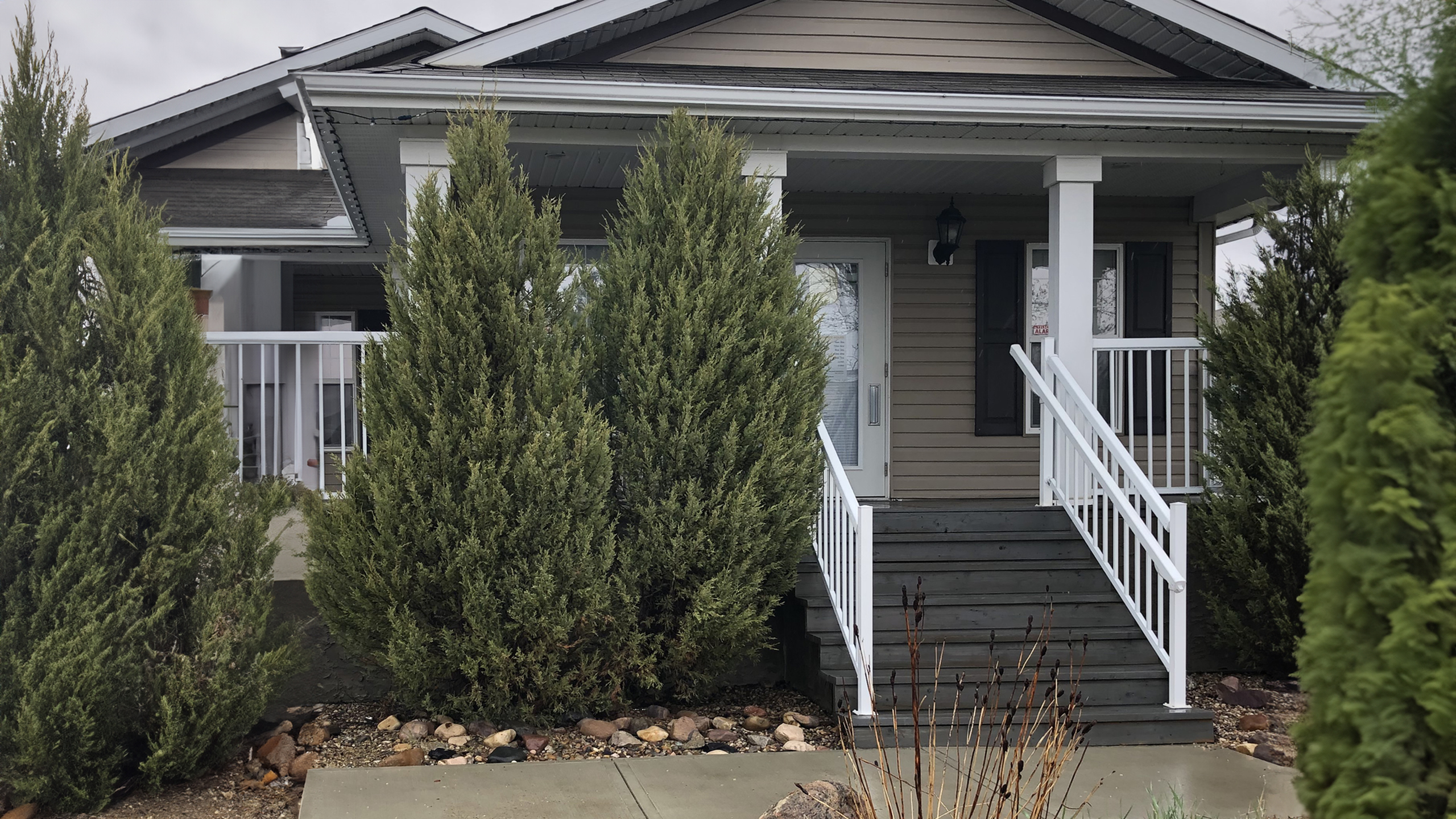 Charming modern home exterior with inviting front porch and elegant landscaping, framed by lush evergreen trees.