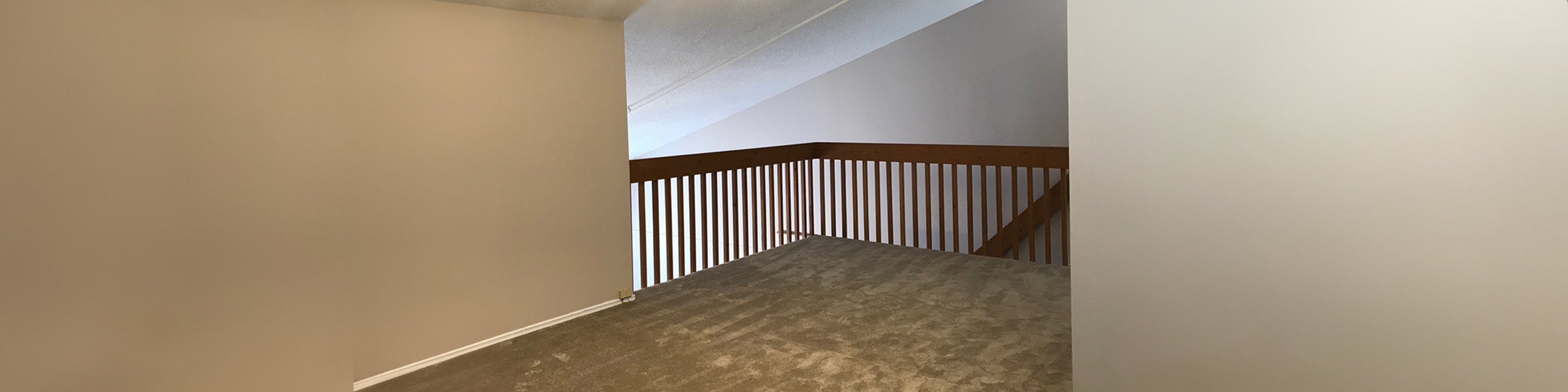 Elegant loft space with plush carpeting and modern wooden railing, offering a cozy nook that overlooks the living area.