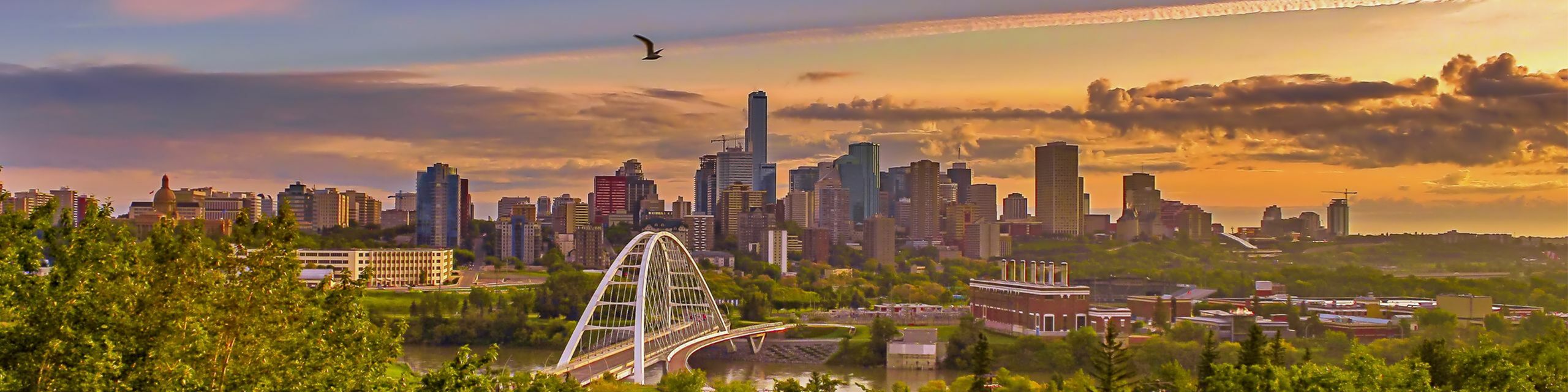 Breathtaking panoramic cityscape with a vibrant skyline at sunset, showcasing modern architecture and a scenic bridge over a lush, green landscape.