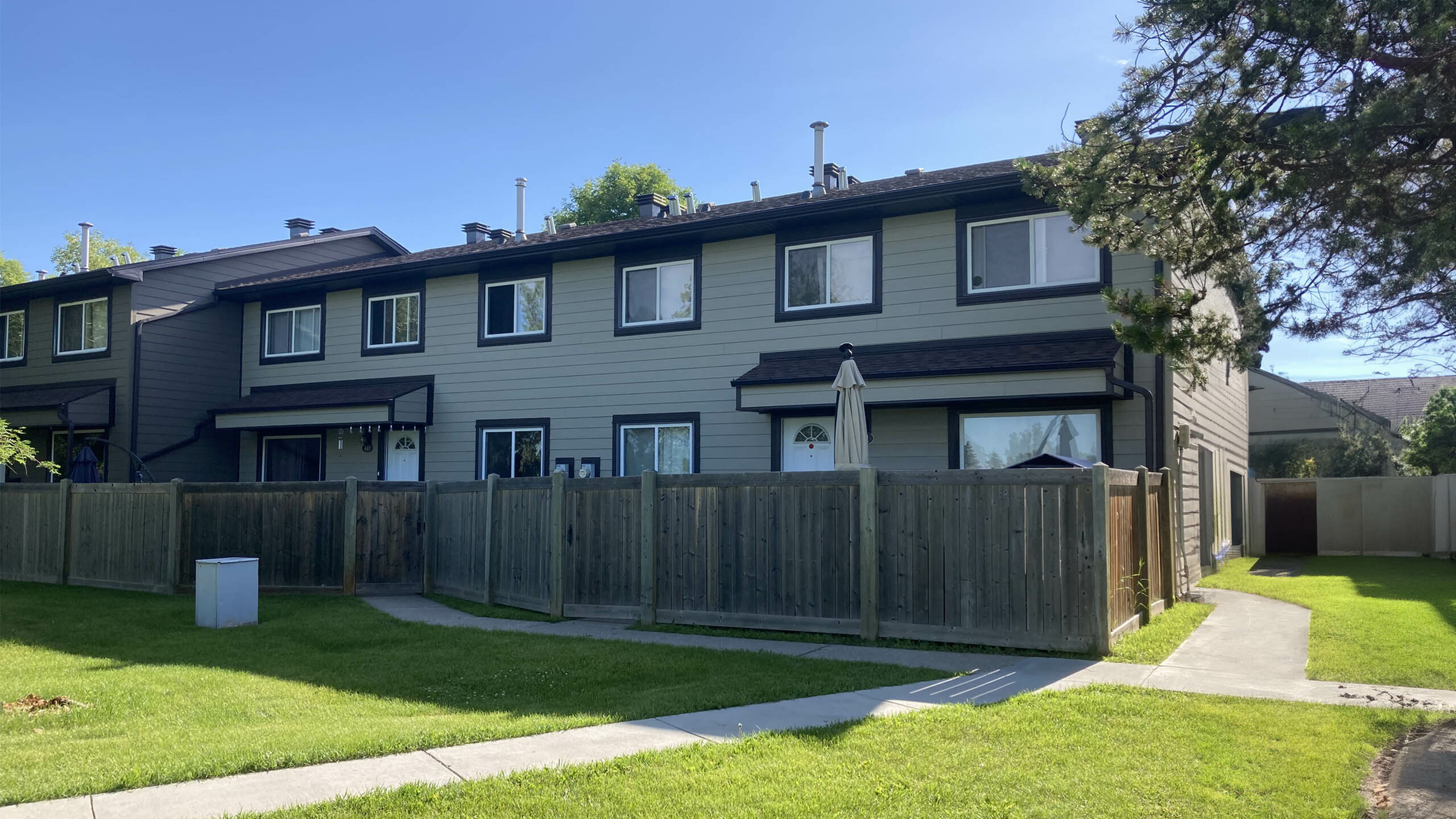 Charming townhouse exterior featuring fenced yards, lush green lawns, and sunny pathways in a serene neighborhood setting.