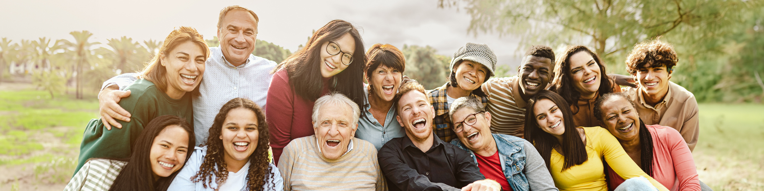 Vibrant group of diverse people smiling joyfully in a lush outdoor setting, showcasing happiness and community spirit.